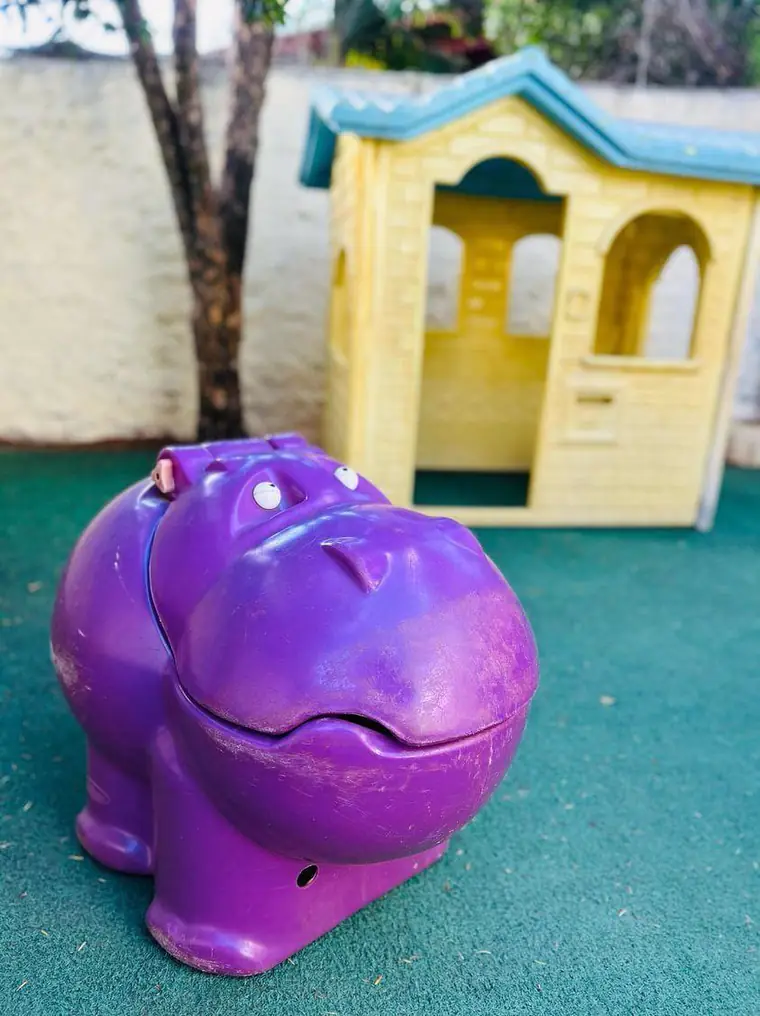 Casinha de brinquedo e gangorra de hipopótamo no gramado sintético