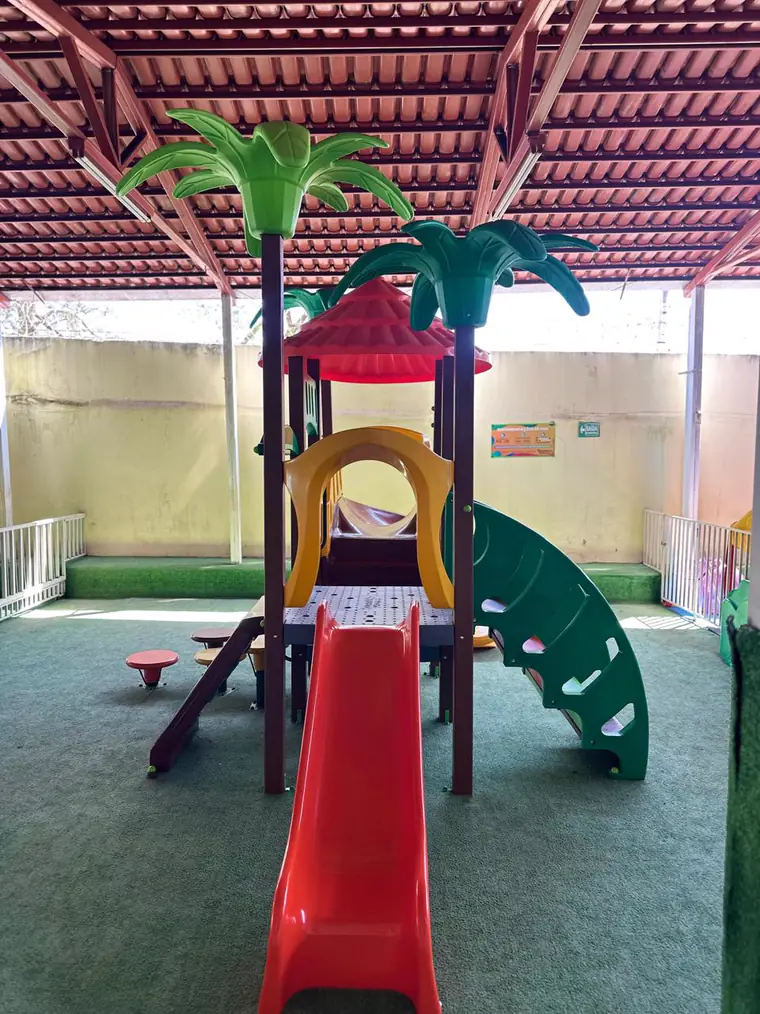 Playground com escorregador e estrutura de palmeiras no pátio coberto