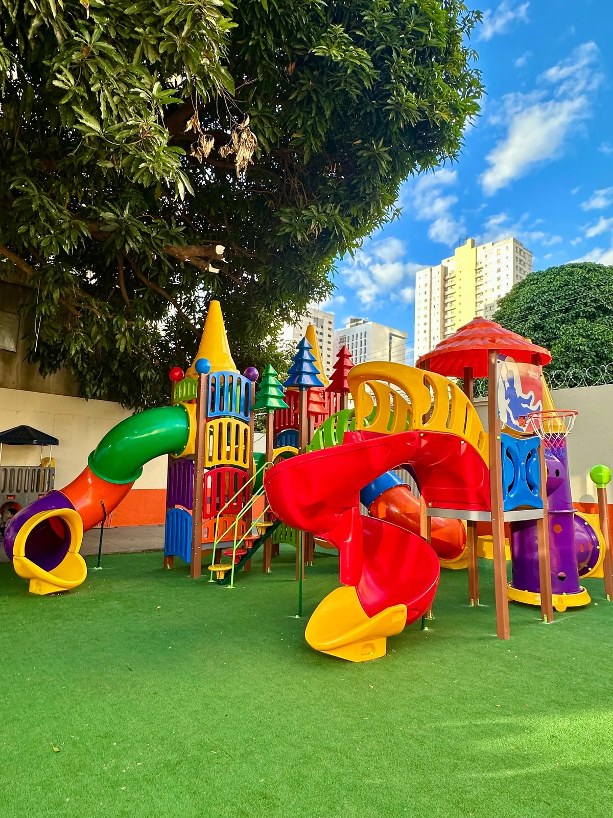 O brinquedão visto do outro lado do pátio, com o escorregador em espiral e a mangueira ao fundo