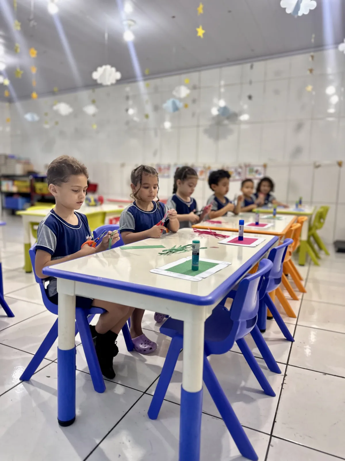 Turma da Criarte III recortando papel nas mesas da sala, com o teto decorado de nuvens e estrelas