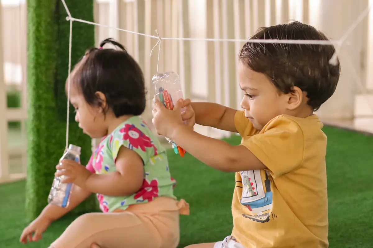 Duas crianças sentadas na grama brincando com garrafas sensoriais