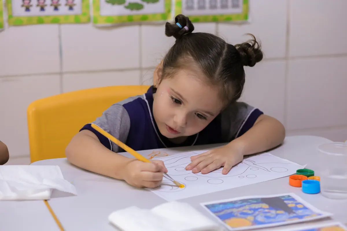 Menina concentrada pintando com tinta guache na sala de aula