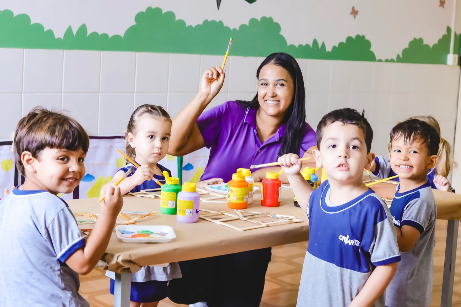 Professora da Criarte I com quatro crianças pintando palitos na mesa da sala
