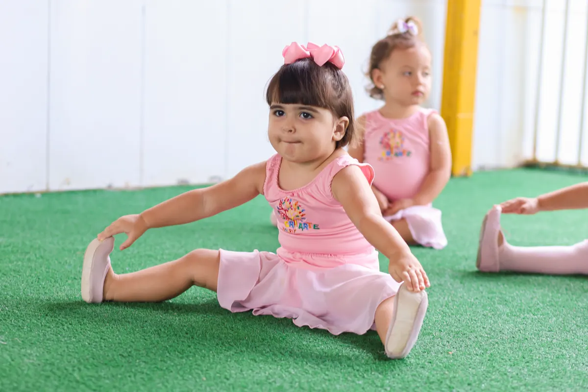 Menina de uniforme rosa fazendo alongamento na aula de balé da Criarte I