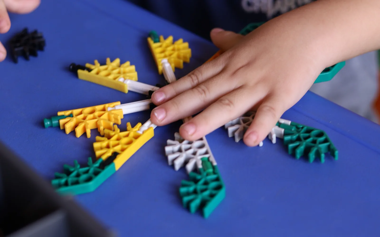 Mão de um aluno da Criarte montando peças de encaixe amarelas e verdes na mesa, na aula de cultura maker