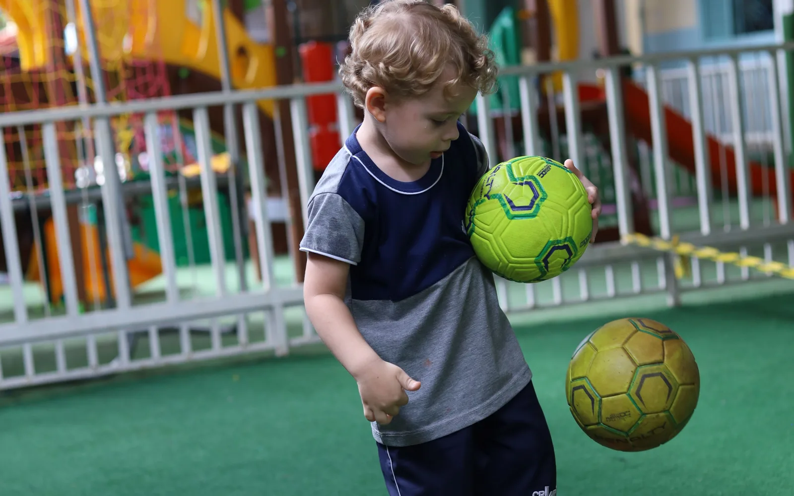 Menino de uniforme Criarte segurando uma bola na área externa da escola, na aula de educação física